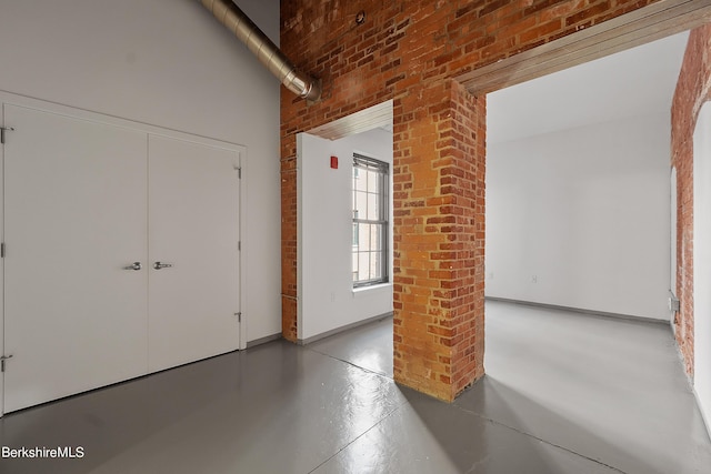 interior space with decorative columns, a high ceiling, brick wall, and concrete floors