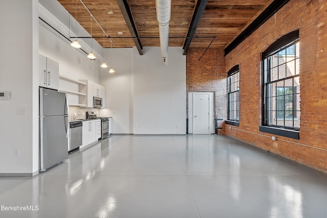 kitchen featuring brick wall, stainless steel appliances, white cabinets, a high ceiling, and hanging light fixtures