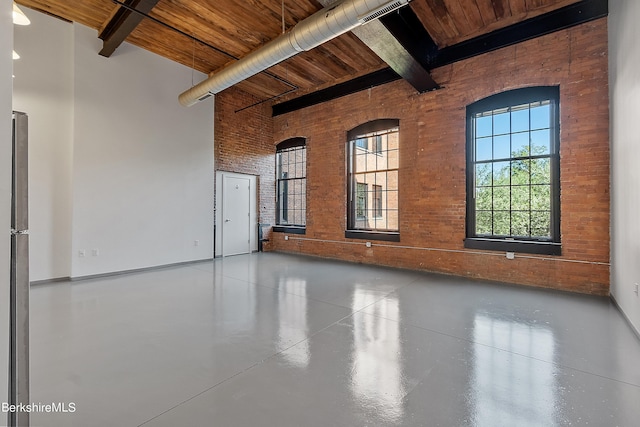 spare room with beamed ceiling, a towering ceiling, wood ceiling, and brick wall