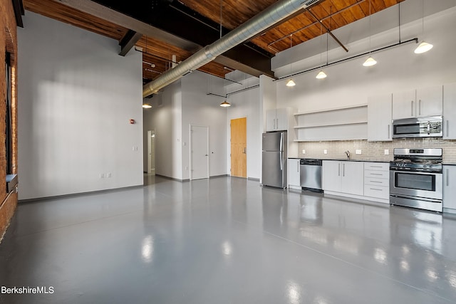 interior space with appliances with stainless steel finishes, a towering ceiling, backsplash, decorative light fixtures, and white cabinetry