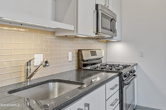 kitchen with appliances with stainless steel finishes, backsplash, dark stone counters, sink, and white cabinetry