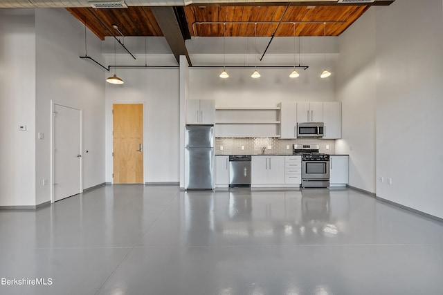 kitchen featuring appliances with stainless steel finishes, a towering ceiling, tasteful backsplash, white cabinetry, and hanging light fixtures