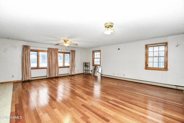 empty room featuring a baseboard heating unit, a healthy amount of sunlight, baseboards, and light wood-style floors