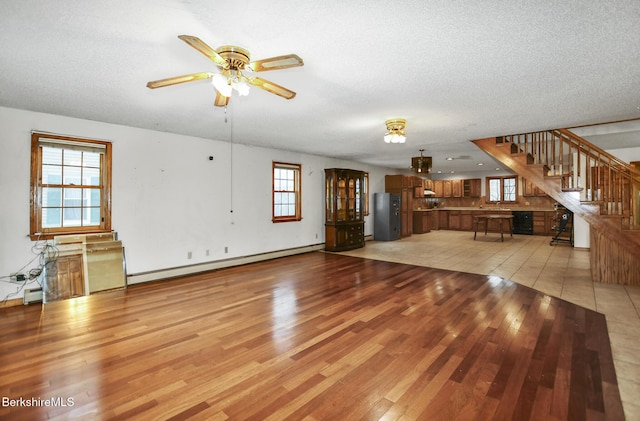 unfurnished living room featuring a ceiling fan, stairs, a textured ceiling, light wood-type flooring, and a baseboard heating unit