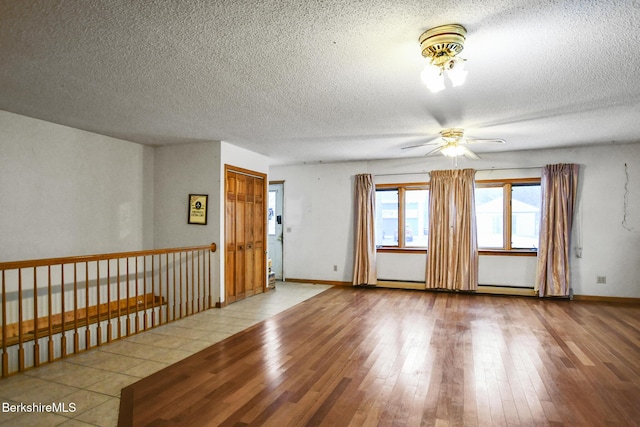 spare room with ceiling fan, a textured ceiling, baseboards, and wood finished floors