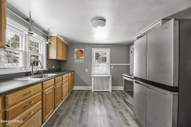 kitchen with appliances with stainless steel finishes, tasteful backsplash, radiator, sink, and wood-type flooring