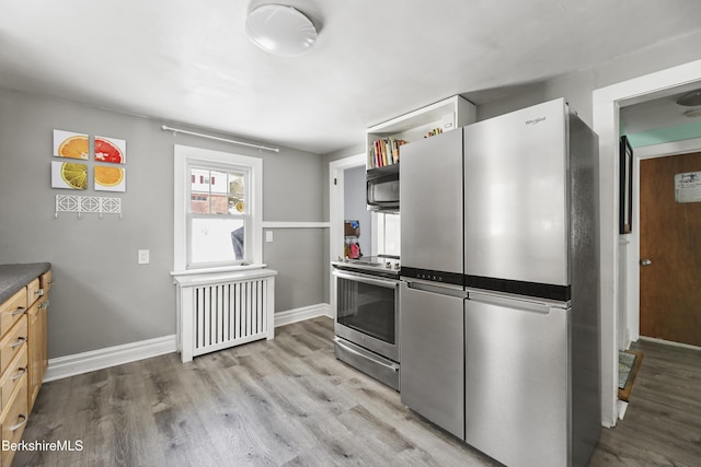 kitchen with radiator heating unit, light hardwood / wood-style flooring, stainless steel appliances, and light brown cabinets