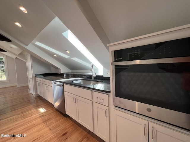 kitchen with white cabinets, appliances with stainless steel finishes, lofted ceiling with skylight, and sink