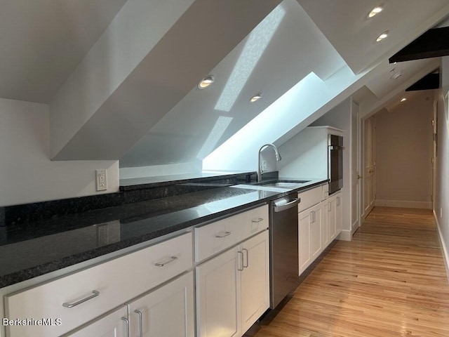 kitchen featuring a skylight, white cabinetry, sink, stainless steel appliances, and dark stone countertops