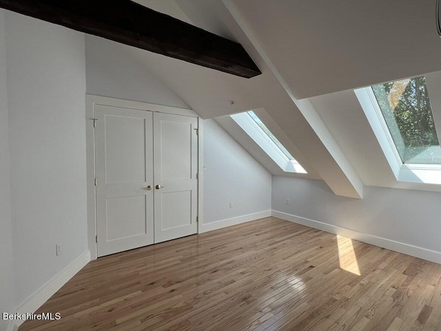 additional living space featuring vaulted ceiling with skylight and light hardwood / wood-style floors