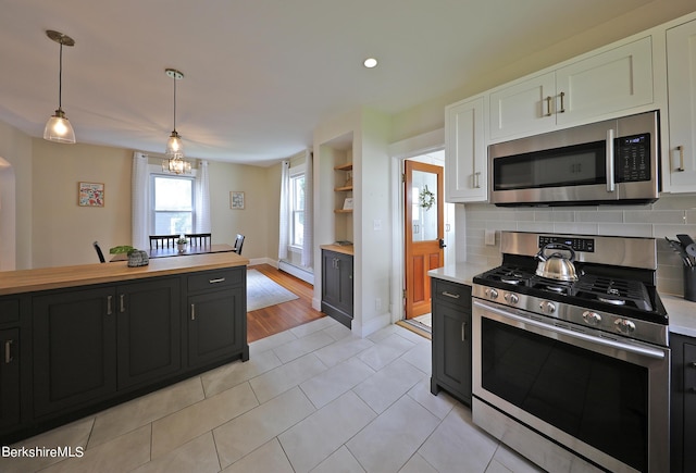 kitchen with pendant lighting, light tile patterned floors, baseboard heating, white cabinetry, and stainless steel appliances