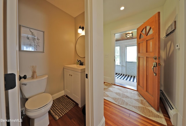 bathroom featuring vanity, toilet, wood-type flooring, and a baseboard heating unit