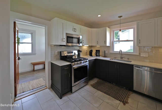 kitchen with stainless steel appliances, sink, pendant lighting, light tile patterned floors, and white cabinetry