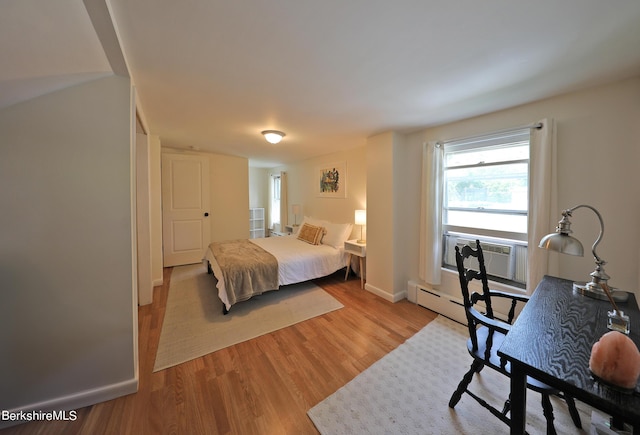 bedroom featuring cooling unit, a baseboard heating unit, and light hardwood / wood-style flooring