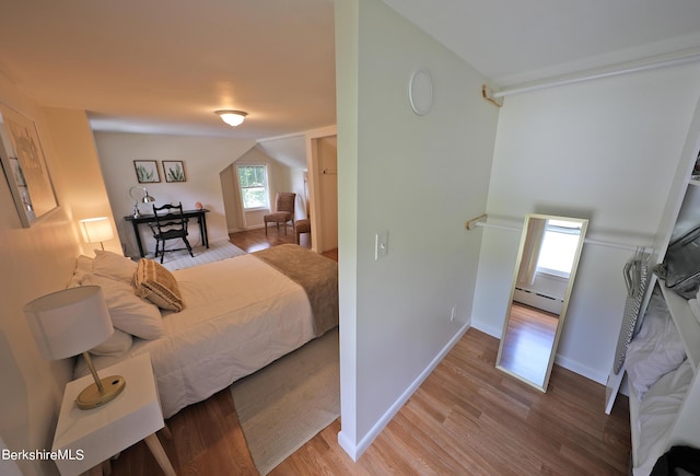 bedroom with hardwood / wood-style flooring, vaulted ceiling, and a baseboard heating unit