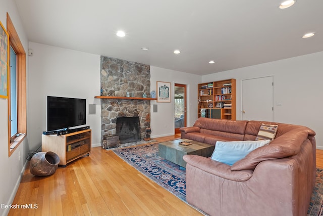 living area with baseboards, wood-type flooring, recessed lighting, and a stone fireplace