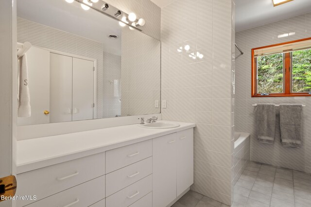 bathroom featuring tiled shower / bath combo, tile walls, tile patterned flooring, and vanity