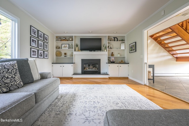 living room featuring built in shelves, a brick fireplace, a baseboard heating unit, crown molding, and hardwood / wood-style flooring