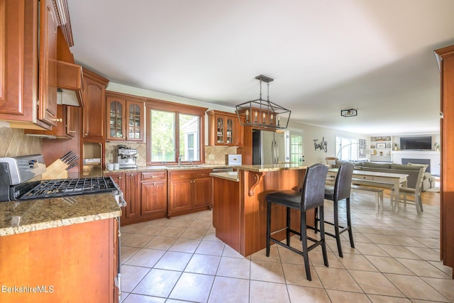 kitchen with stainless steel refrigerator, a center island, sink, decorative light fixtures, and light tile patterned floors