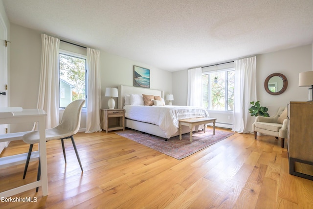 bedroom featuring baseboard heating, a textured ceiling, and light hardwood / wood-style flooring