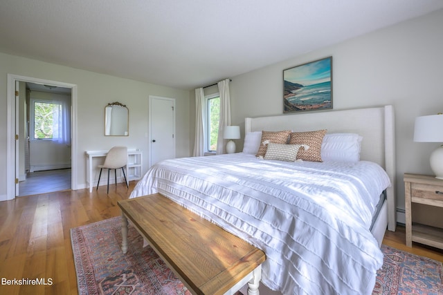 bedroom featuring baseboard heating, multiple windows, and wood-type flooring