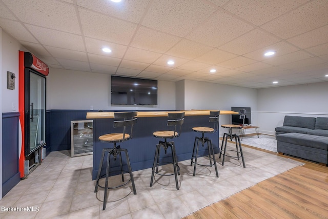 bar with a drop ceiling, beverage cooler, and light hardwood / wood-style flooring