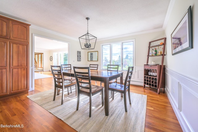 dining area with hardwood / wood-style flooring, crown molding, a textured ceiling, and an inviting chandelier