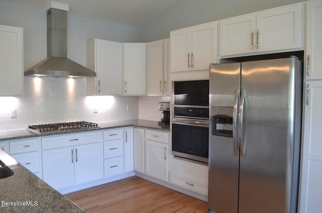 kitchen with wall chimney exhaust hood, dark stone countertops, white cabinetry, and appliances with stainless steel finishes