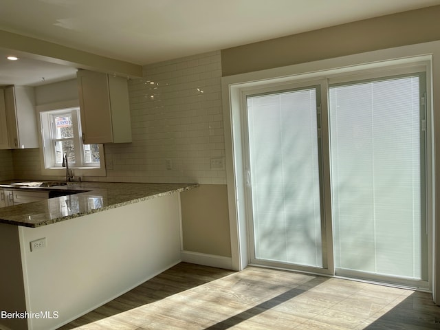 kitchen featuring decorative backsplash, dark stone countertops, light wood-type flooring, and a sink