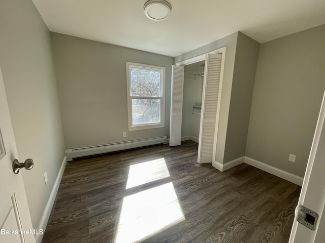 unfurnished bedroom featuring a closet, baseboard heating, baseboards, and wood finished floors