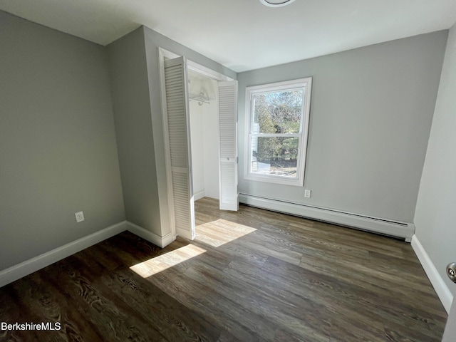 unfurnished bedroom featuring a baseboard heating unit, baseboards, and wood finished floors