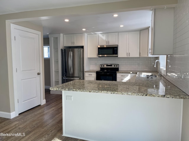 kitchen with light stone countertops, dark wood finished floors, decorative backsplash, stainless steel appliances, and a sink