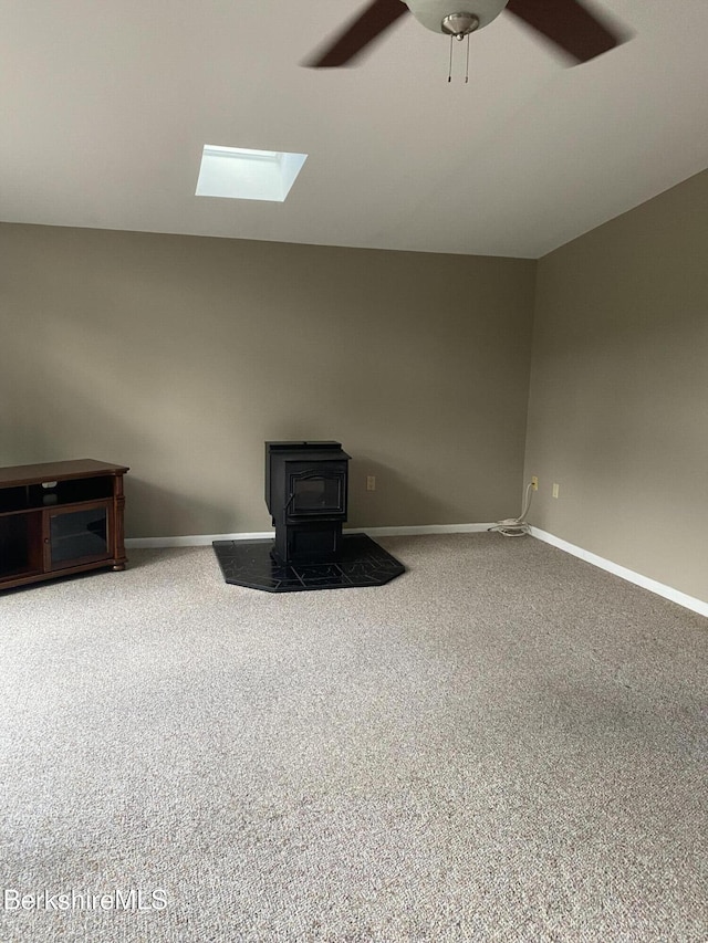 1050 Cape St, Lee, MA 01238 - unfurnished living room featuring carpet flooring, a wood stove, ceiling fan, and a skylight