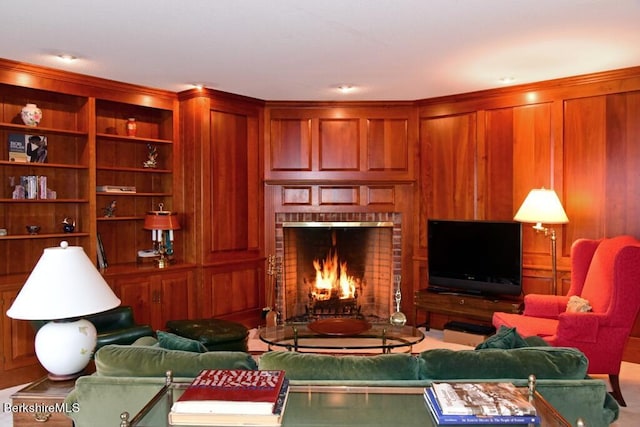 living room with built in shelves, wood walls, and a brick fireplace