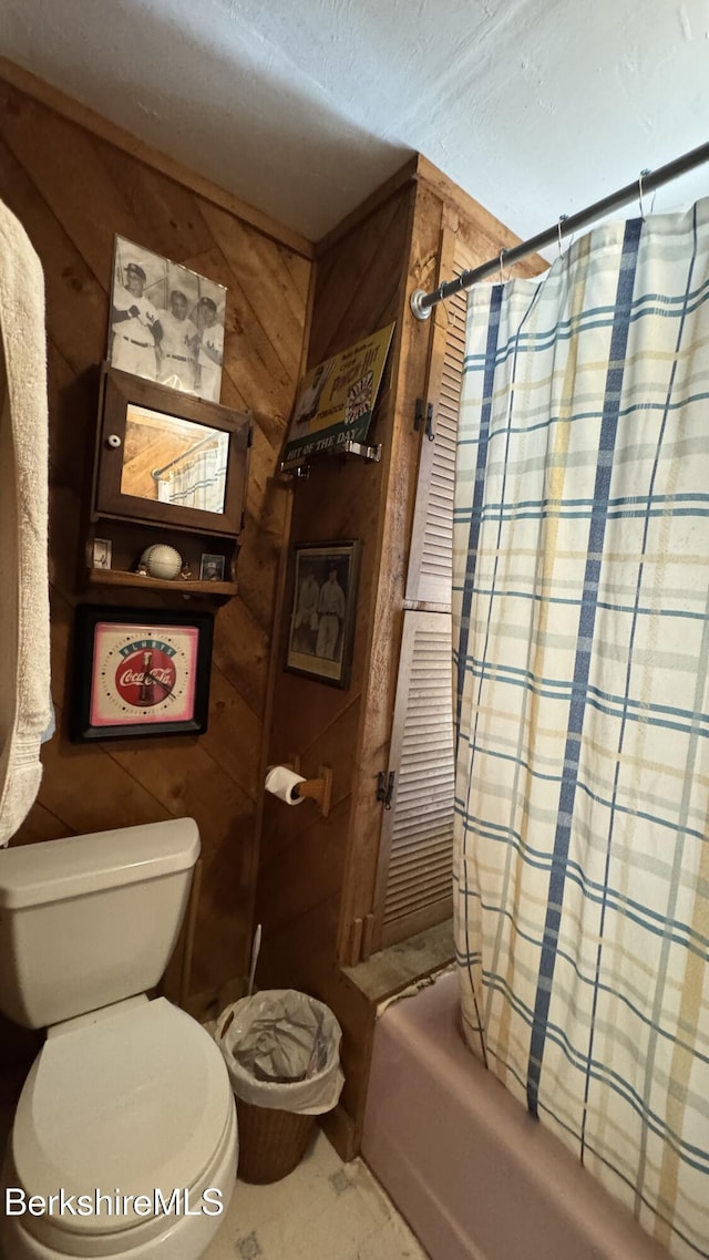 bathroom featuring shower / bath combo with shower curtain, wood walls, a textured ceiling, and toilet