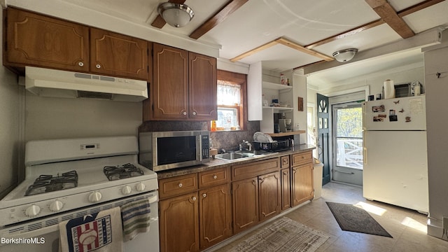 kitchen featuring backsplash, dark countertops, a sink, under cabinet range hood, and white appliances