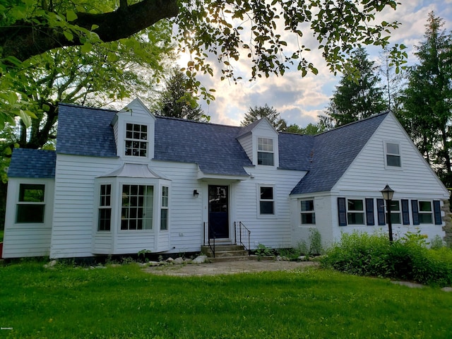 cape cod-style house with a front lawn, roof with shingles, and entry steps