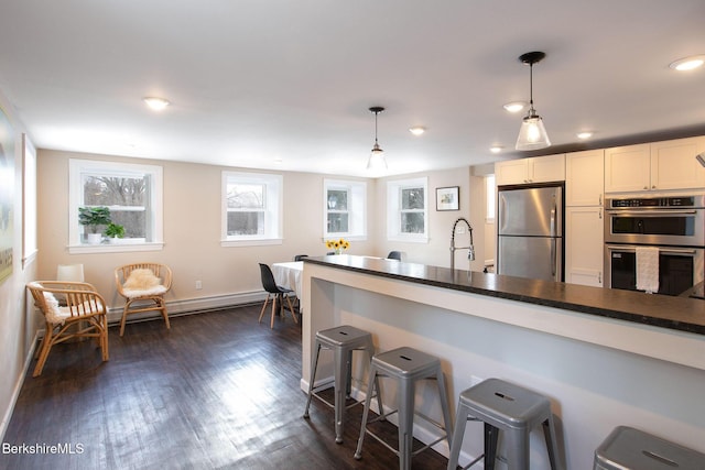 kitchen with a breakfast bar, white cabinetry, hanging light fixtures, appliances with stainless steel finishes, and dark hardwood / wood-style floors