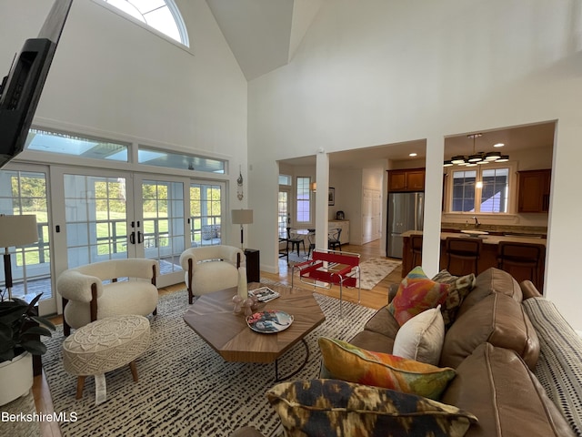 living room featuring high vaulted ceiling, french doors, sink, light hardwood / wood-style flooring, and ceiling fan