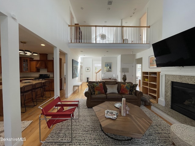 living room featuring ceiling fan, a fireplace, light hardwood / wood-style floors, and a high ceiling