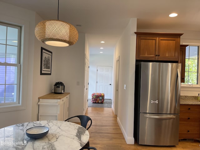 kitchen featuring stainless steel fridge, light wood-type flooring, light stone countertops, and hanging light fixtures