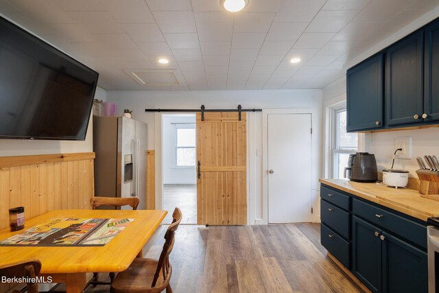 kitchen featuring blue cabinetry, a barn door, light hardwood / wood-style floors, and stainless steel refrigerator with ice dispenser