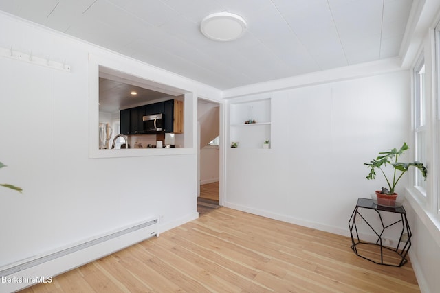 spare room featuring built in shelves, sink, baseboard heating, wood-type flooring, and ornamental molding