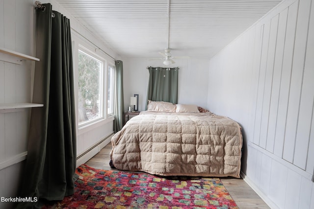 bedroom with ceiling fan, light hardwood / wood-style floors, and a baseboard heating unit