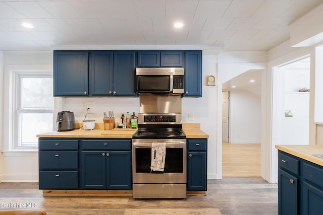 kitchen featuring blue cabinetry, light hardwood / wood-style flooring, stainless steel appliances, and wood counters