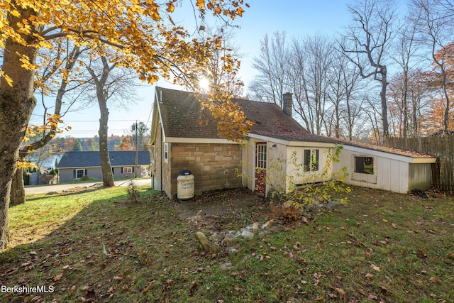back of house with a shingled roof, a chimney, and a yard