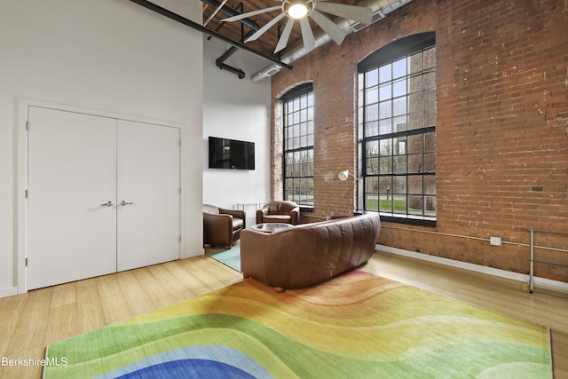 living room with ceiling fan, a towering ceiling, brick wall, and wood-type flooring