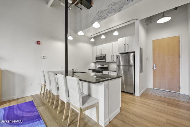 kitchen featuring white cabinetry, sink, a high ceiling, a breakfast bar, and appliances with stainless steel finishes