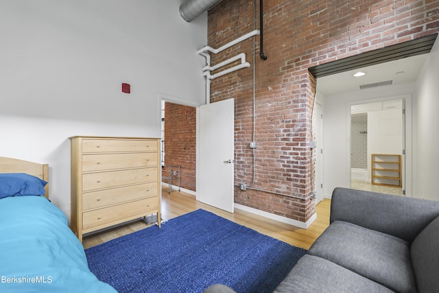 bedroom with a towering ceiling, brick wall, and light wood-type flooring