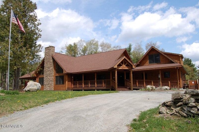 log home featuring covered porch, driveway, a front lawn, and a chimney